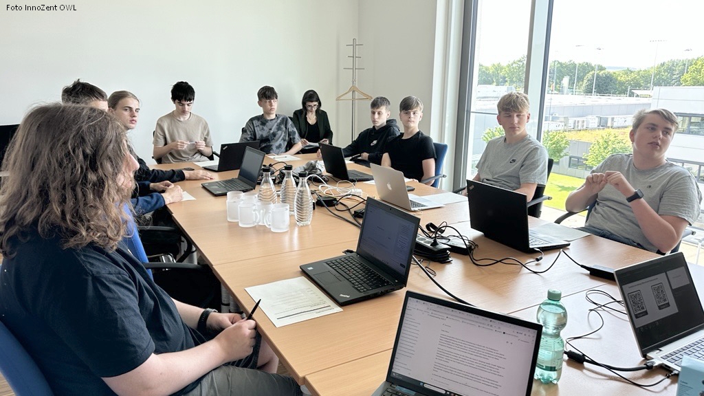 Größere Gruppe Jugendlicher sitzt mit Laptops am Konferenztisch und diskutiert im Rahmen des KI-Workshops