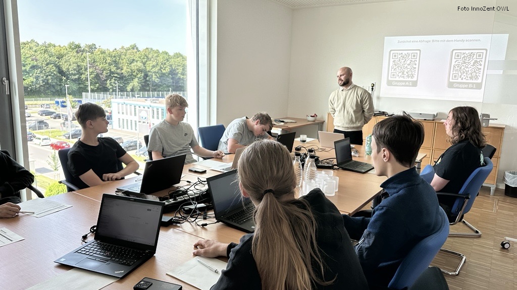 Jugendliche mit Laptops im Seminarraum, im Hintergrund Referent und Projektion mit QR-Codes zur Gruppenaufteilung